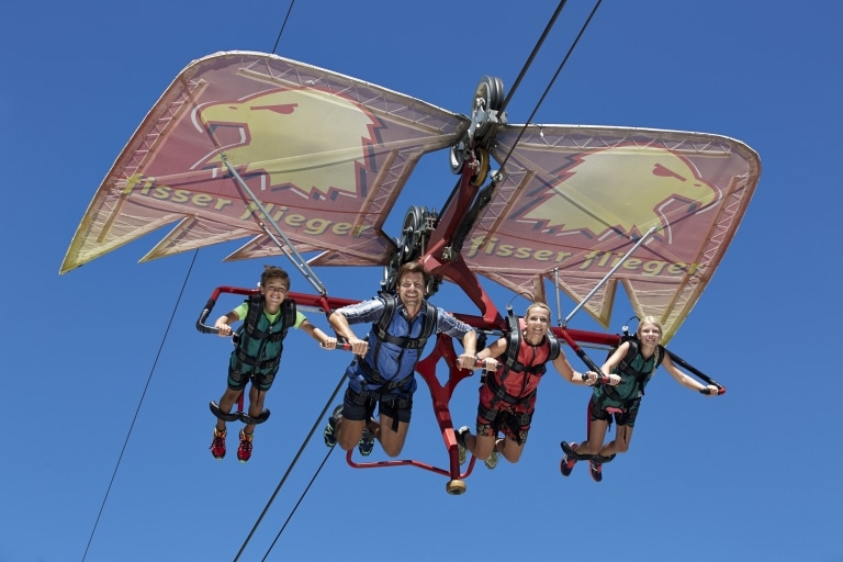 Zwei Kinder sowie zwei Erwachsene hängen am Fisser Flieger, einer drachenähnlichen Flugkonstruktion im Funpark Fiss in Tirol.
