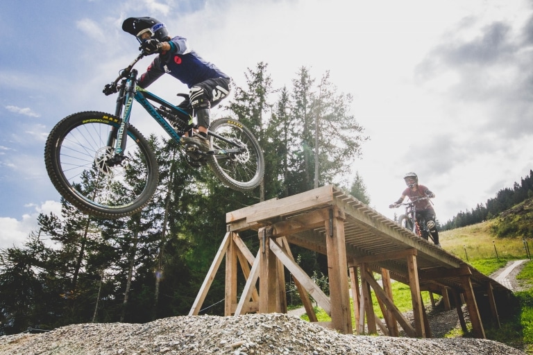 Mountainbiker springt im Downhill Park in Fiss in Tirol von einer Holzkonstruktion. Der Bikepark ist nur wenige Minuten von unserem Mountainbikehotel entfernt.