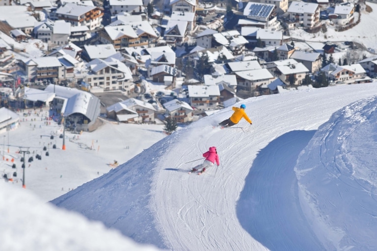 Zwei Skifahrer mit Blick auf ein Dorf im Tal