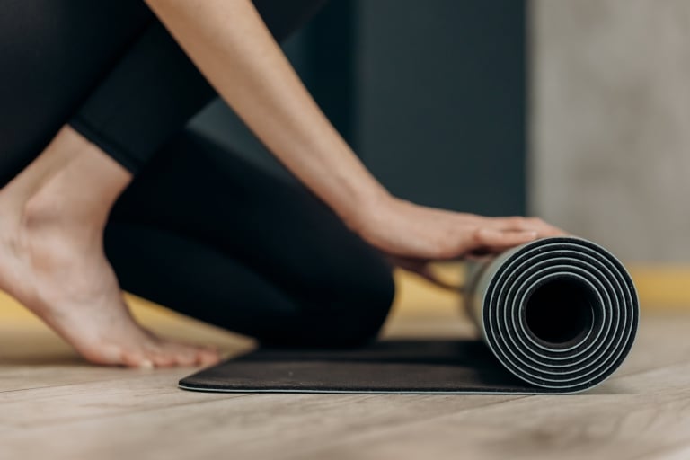 Schwarze Yoga-Matte eingerollt auf einem Holzboden