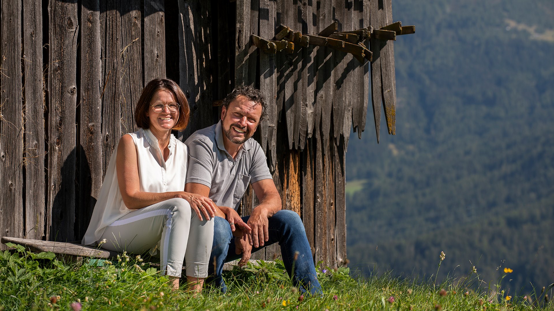 Gastgeber Familie Pregenzer lächelnd vor einer Hütte sitzend im Sommer
