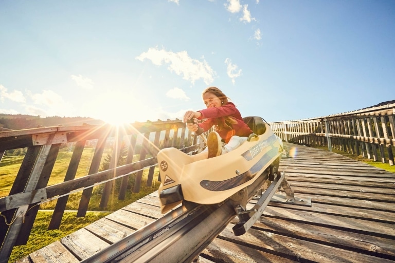Mädchen fährt auf der Sommerrodelbahn Fisser Flitzer im Funpark Fiss-Serfaus-Ladis den Hang hinab.