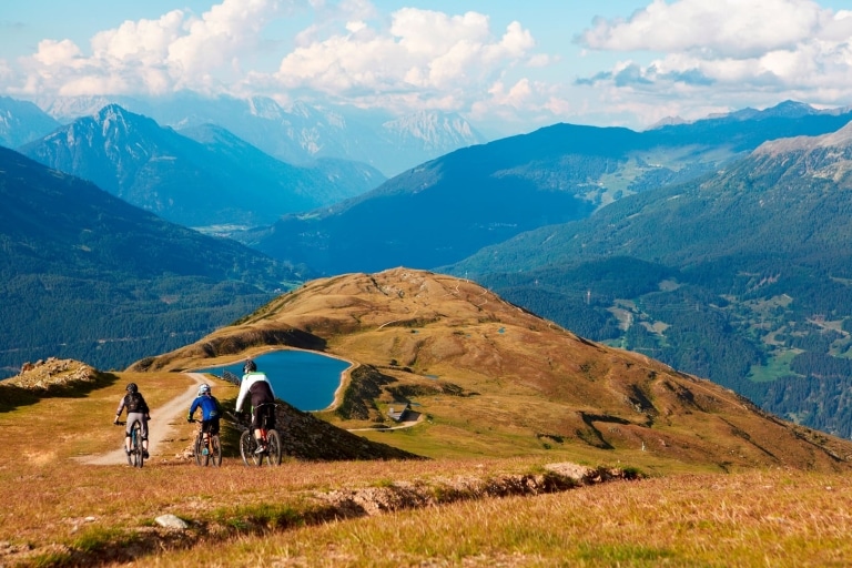 Drei Mountainbiker fahren einen Hang in Tirol hinab.