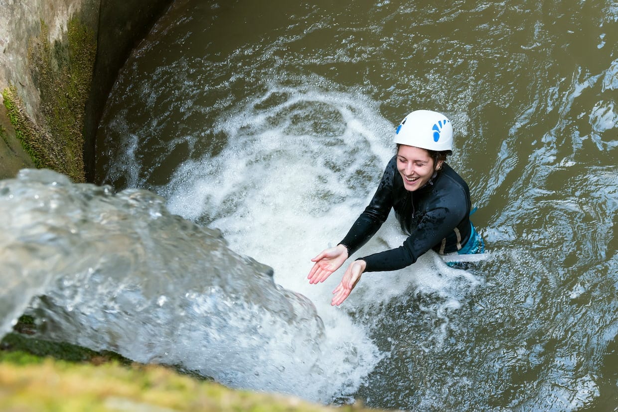 Lächelnde Frau steht beim Canyoning in Tirol mit offenen Armen vor einem Wasserfall.